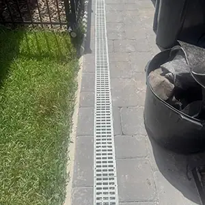 Channel drain grate set into pavers beside a lawn