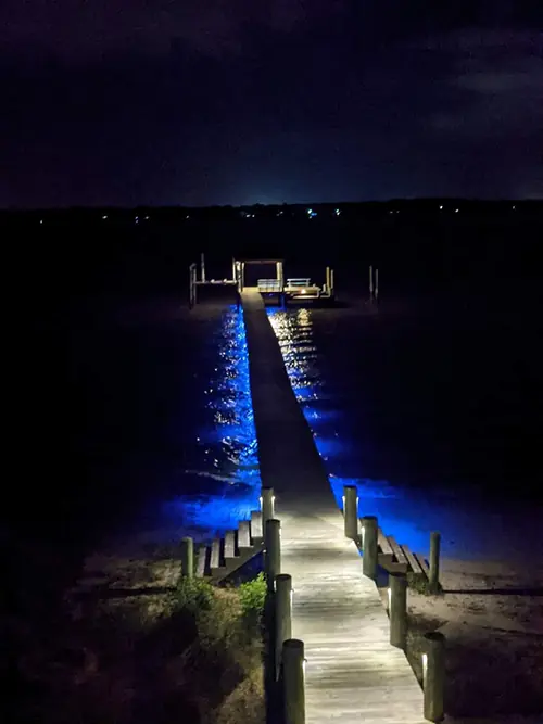 Long dock lit blue along both edges, stretching out over dark water