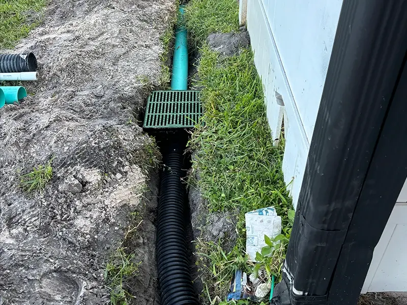 Trench along a house with drain pipe and a catch basin being installed by Zuzack