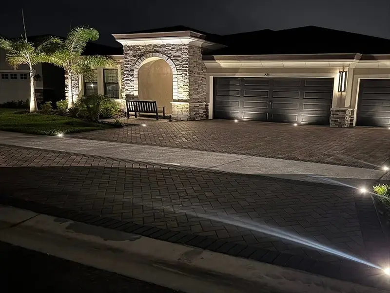 Driveway and garage lit by warm wall lights and in-ground lights