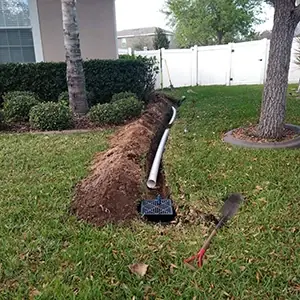 French drain trench across a lawn with white perforated pipe and a catch basin
