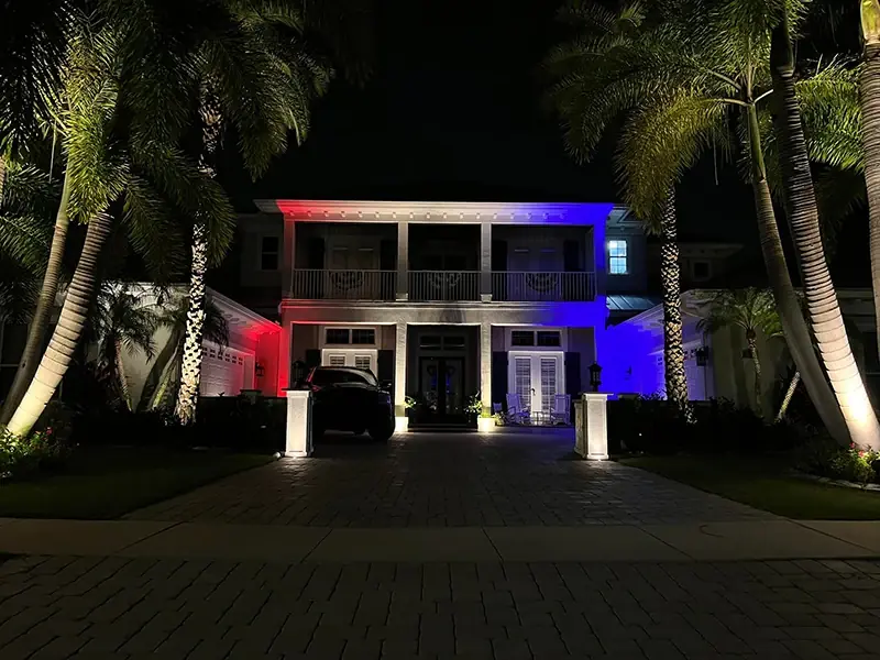 Two-story home lit red, white and blue between palm trees