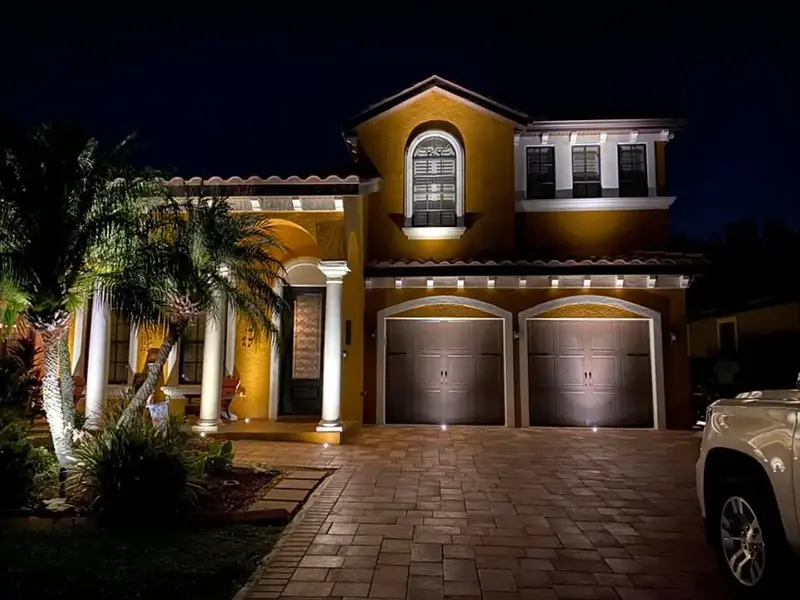 Two-story home with warm light on the columns, balcony and garage at night