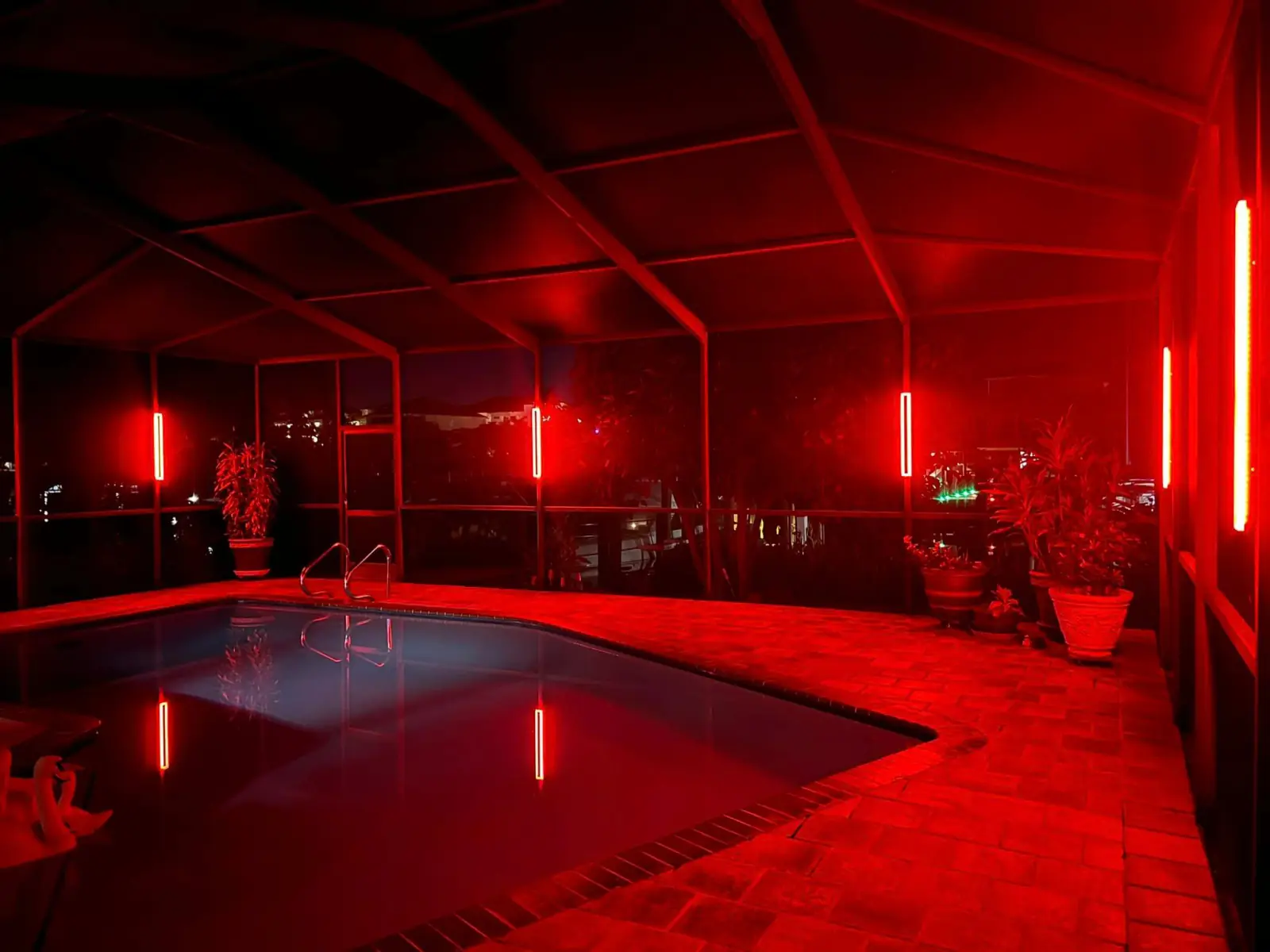 The same Zuzack pool cage lit ember red, reflecting on the water