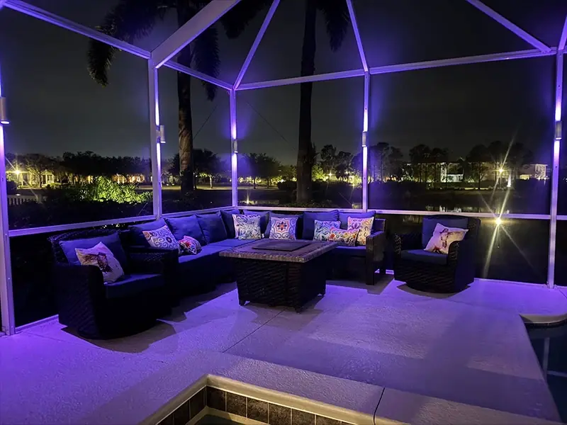 Lanai seating area with sofas and a fire table under purple pool cage lighting