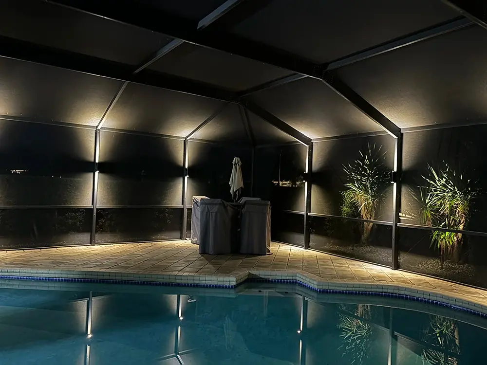 Pool cage at night with warm white light bars reflecting in the pool