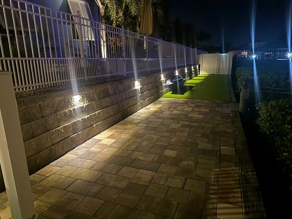 Paver walkway beside a block wall lit by small wall lights at night
