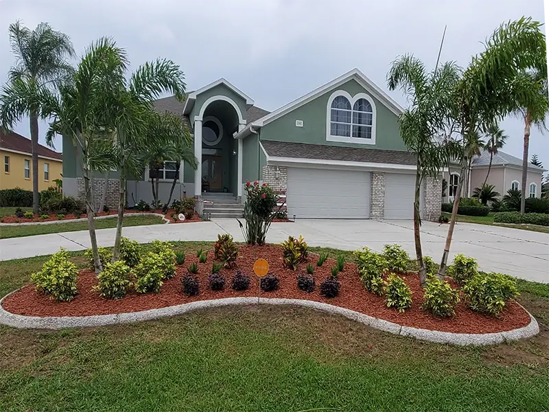 New paver walkway lined with tropical plants and mulch beds beside a lawn