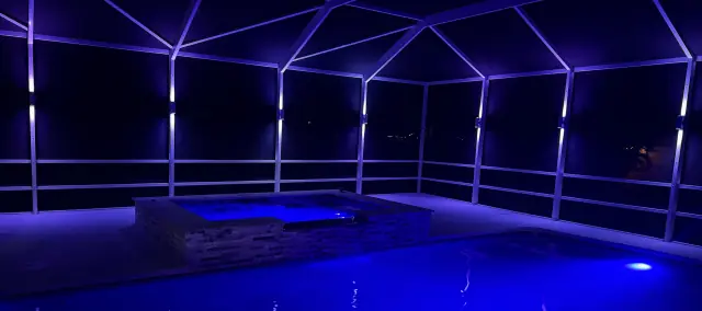 Screened pool cage lit in blue with color light bars along the frame at night