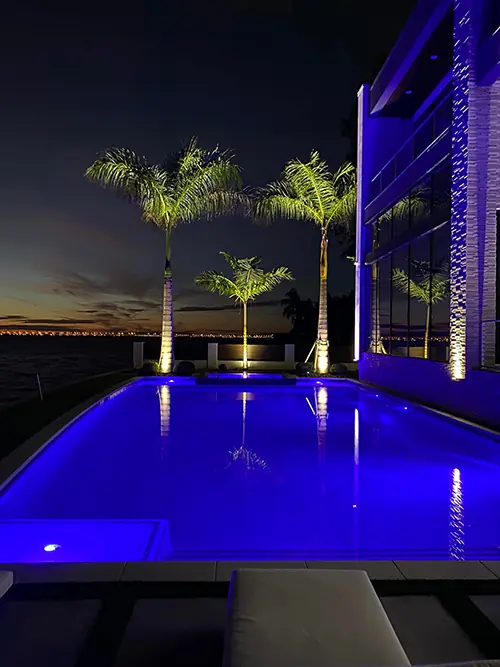 Waterfront pool with up-lit palms and the bay beyond at dusk